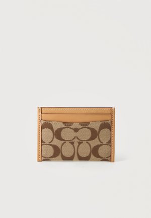Porte-cartes en tissu marron à motifs avec bords et coutures en cuir fauve sur fond clair.