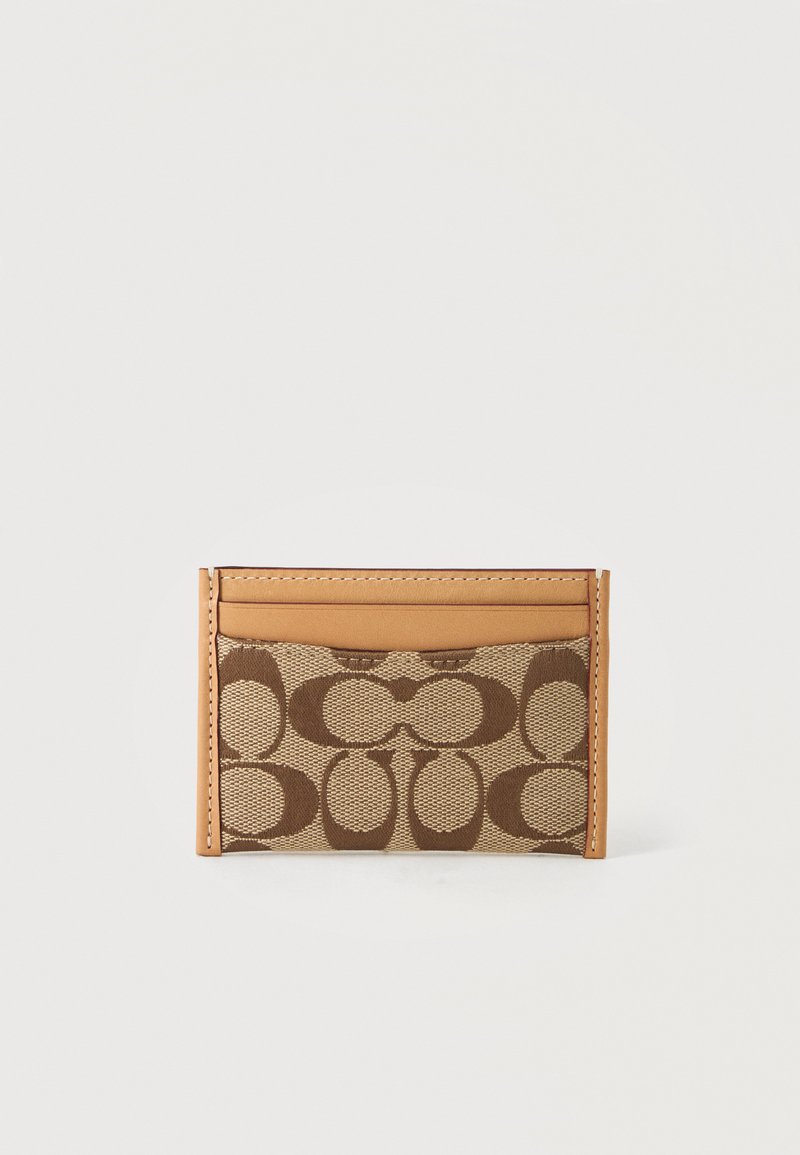 Porte-cartes en tissu marron à motifs avec bords et coutures en cuir fauve sur fond clair.