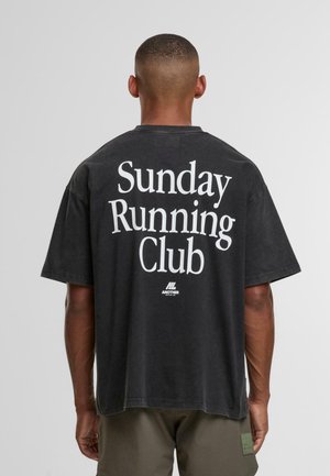Black oversized t-shirt with large white text "Sunday Running Club" on the back. Short sleeves; casual, relaxed fit. Cotton material.