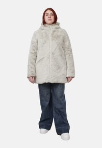 Cappotto con cappuccio in pelliccia sintetica grigio chiaro, dotato di chiusura con zip e maniche lunghe, abbinato a jeans di denim blu a gamba larga e sneakers bianche.