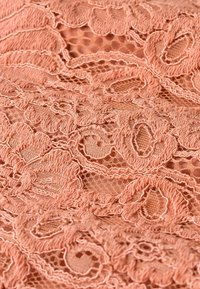 Tissu de dentelle pêche avec un motif floral, présentant une broderie complexe et un tissage ouvert, mettant en valeur des textures douces et des détails délicats.