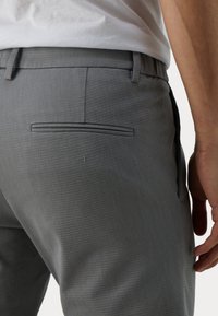 Grå texturerade byxor med slim fit, som har en enda bakficka och bälteshällor, i kombination med en ljusfärgad skjorta.
