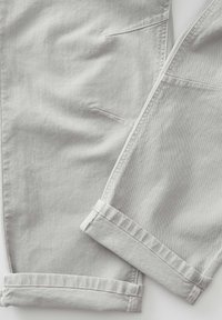 Jean en denim gris clair avec coutures visibles et revers pliés, posé à plat sur une surface blanche.