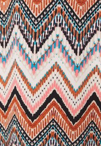 Padrão zigzag multicolorido em tecido apresentando formas castanhas, pretas, rosas e azuis. O fundo é creme com detalhes intrincados.