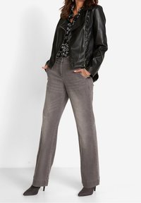 Veste de motard en cuir noir sur une chemise à motifs noir et blanc, associée à un jean gris à jambes larges et des bottines à talons grises.