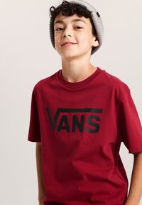 Bordová tričko s krátkým rukávem, které má na přední straně výrazné černé logo "VANS". Tkanina vypadá měkce a hladce, s volným střihem.