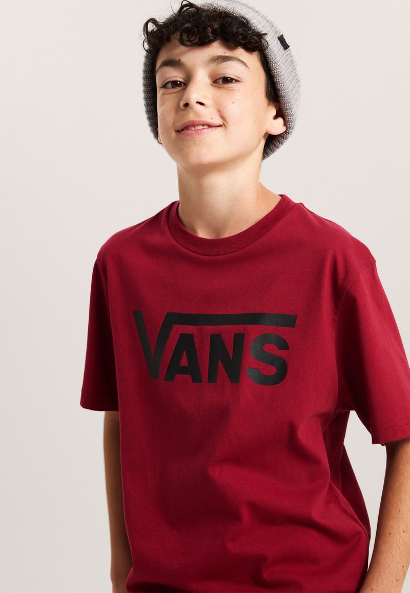 Bordowa koszulka z krótkim rękawem z wyraźnym czarnym logo "VANS" na przodzie. Materiał wydaje się miękki i gładki, z luźnym krojem.