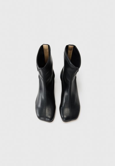 Svarta läderankelboots med en blank yta, avsmalnande fyrkantig tå och en dragkedja på sidan. Inre foder i ett kontrasterande beige material.