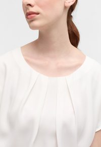 Weißes Blusenshirt mit weitem, abgerundetem Ausschnitt und sanften Falten. Hergestellt aus leichtem Stoff, hat es eine glatte Textur und eine entspannte Passform.