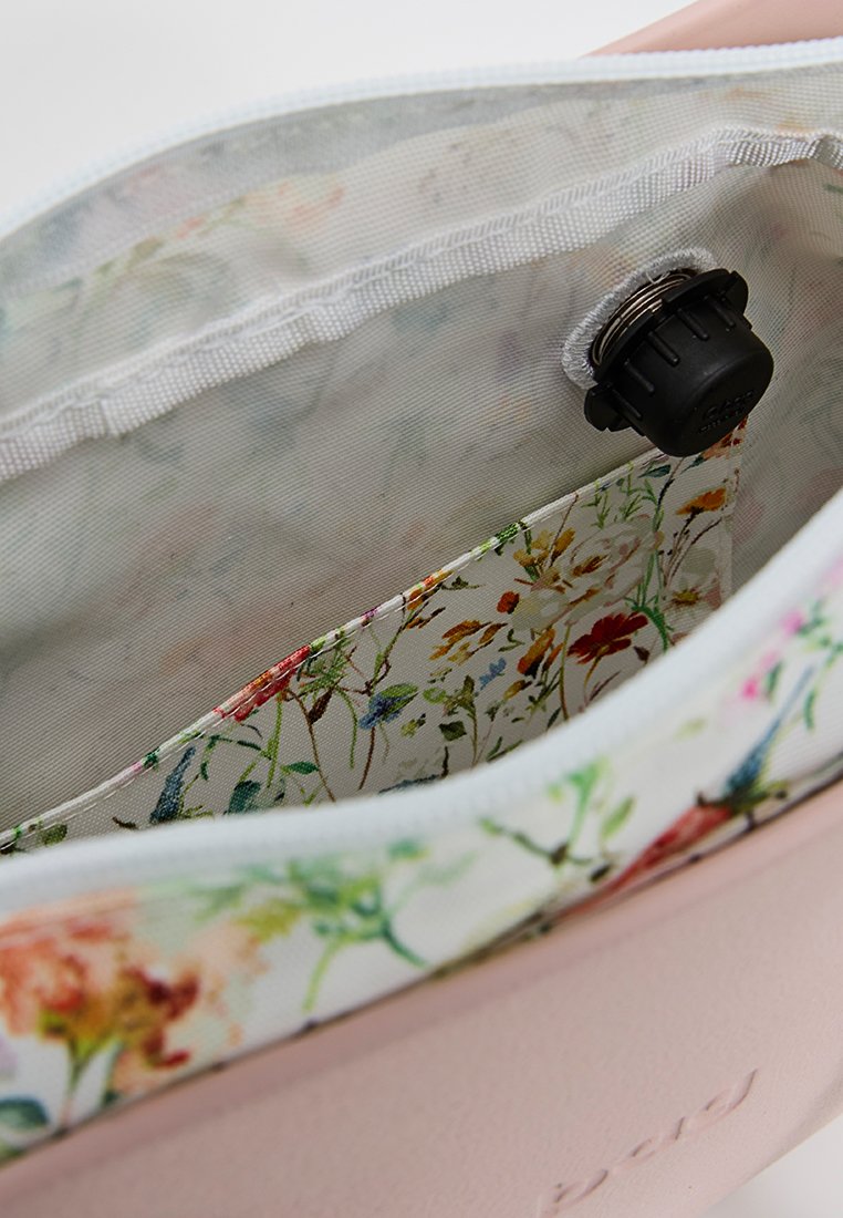 Jasnoróżowe wnętrze torby z podszewką w kwiatowy wzór; posiada zamek błyskawiczny i okrągły czarny zamek.