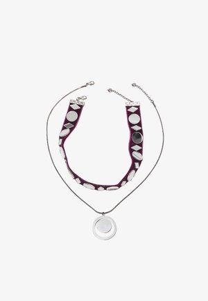 Ogrlica z dvema plastema, ki vključuje srebrno verižico in vijoličen trak iz blaga, okrašen s srebrnimi in črnimi geometrijskimi oblikami; priložen je okrogel obesek.