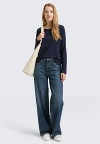 Granatowa bluzka z długim rękawem, luźne jasnoniebieskie szerokie dżinsy i białe trampki, do tego beżowa torba na ramię. Luźny i wygodny strój.