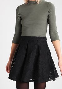 Dark lace skirt with a flared design, featuring a textured floral pattern, paired with a fitted olive green ribbed top and three-quarter sleeves.