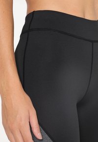 Leggings neri a vita alta con pannelli grigi a contrasto, texture liscia e cuciture piatte per comfort e durata.