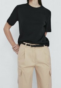 Zwart T-shirt met korte mouwen en een ronde halslijn, gecombineerd met lichtbeige broeken met cargopockets en een gevlochten zwarte riem.