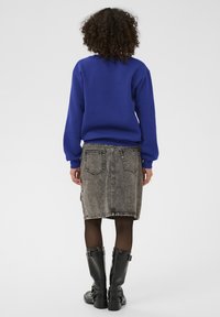 Modrá mikina s kulatým výstřihem, šedá džínsová sukně s přišitými kapsami a černé kozačky po kolena s přezkami, pohled zezadu.