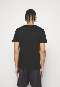 Camiseta negra de manga corta, hecha de algodón y con cuello redondo. La vista trasera muestra una textura suave y sin logotipos ni patrones visibles.