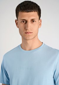 T-shirt azzurro chiaro a maniche corte, realizzata in tessuto morbido, con scollo rotondo e logo "Lindbergh" in rilievo sul davanti.