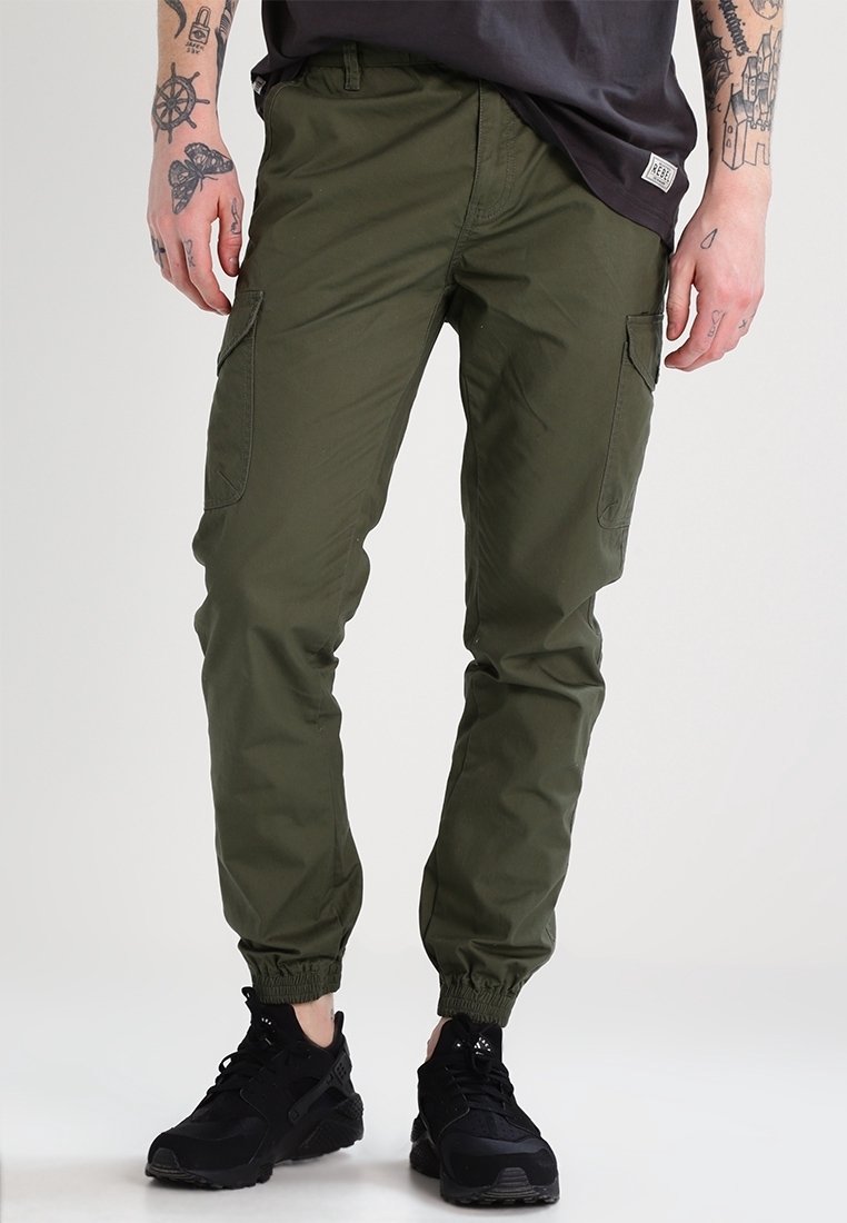 Olivgröna cargobyxor i en bomullsblandning, med elastiska muddar, flera sidofickor och en avslappnad passform. Matchas med svarta sneakers.