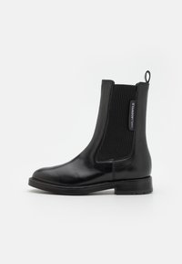 Black leather Chelsea boot featuring elastic side panels, a smooth finish, and a pull tab. The sole is flat with a modest tread.