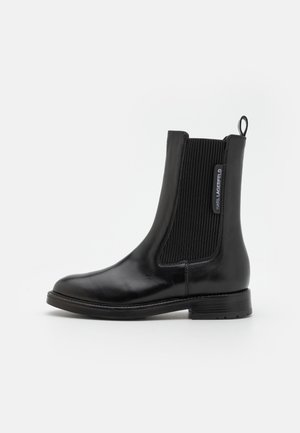 Black leather Chelsea boot featuring elastic side panels, a smooth finish, and a pull tab. The sole is flat with a modest tread.