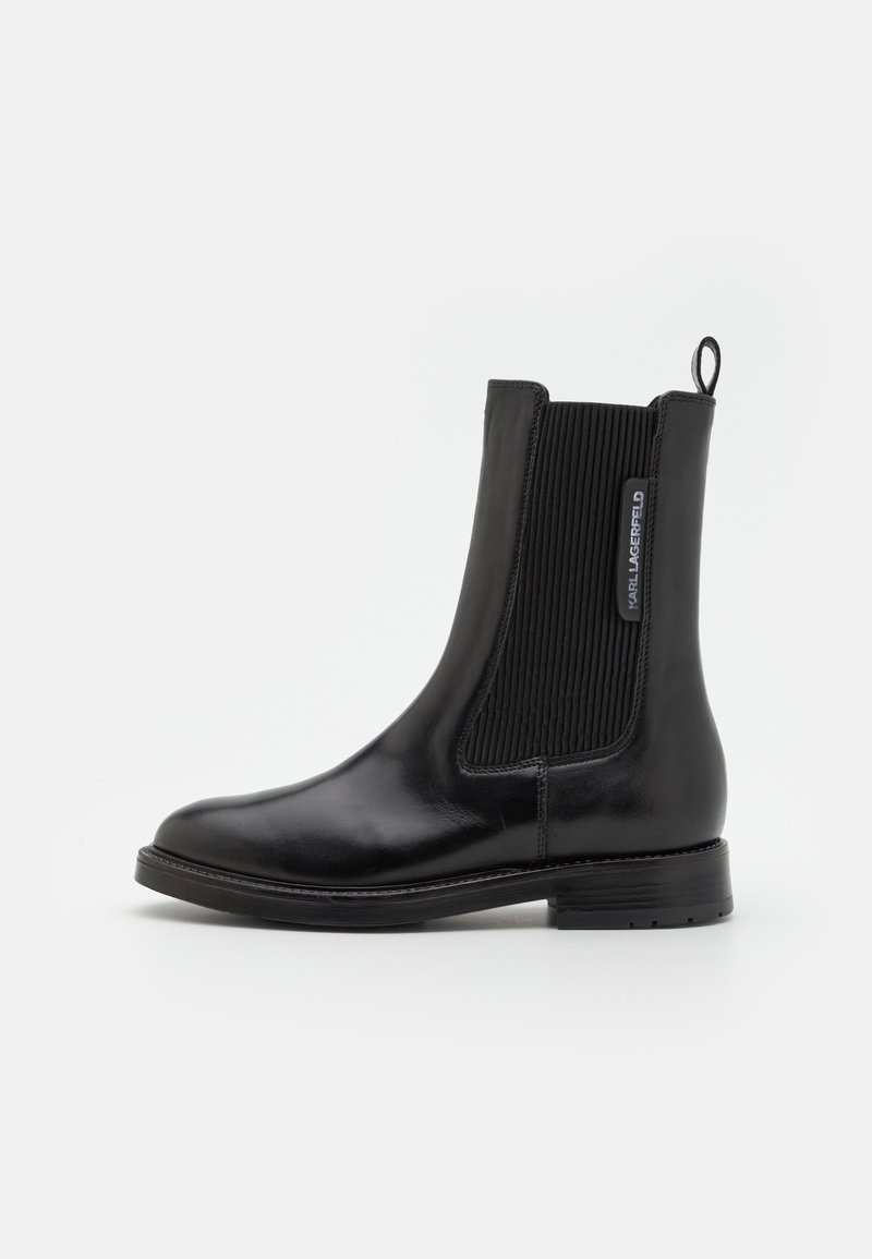 Black leather Chelsea boot featuring elastic side panels, a smooth finish, and a pull tab. The sole is flat with a modest tread.