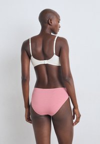 Light beige bra with adjustable straps and a hook closure, paired with pink high-waisted panties, showcasing smooth fabric and simple design.