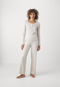 Hellbeige Langarmshirt mit rundem Ausschnitt, Knopfverschluss und strukturiertem Rippstrick; passende weit geschnittene Hose mit Rüschensäumen.