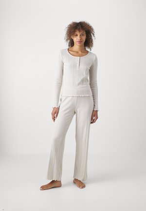 Light beige long-sleeve top with a round neckline, button closure, and textured ribbing; matching wide-leg pants with ruffled hems.