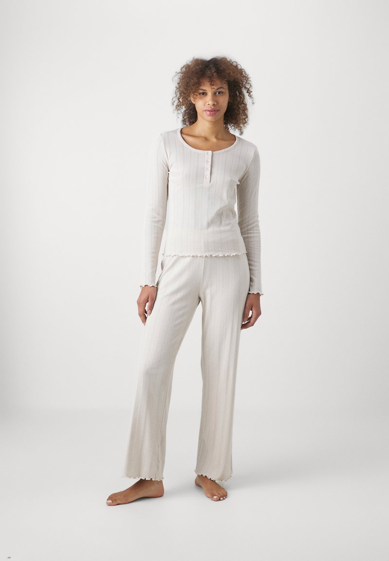 Hellbeige Langarmshirt mit rundem Ausschnitt, Knopfverschluss und strukturiertem Rippstrick; passende weit geschnittene Hose mit Rüschensäumen.