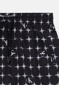 Svarte shorts med et hvitt rutenettmønster, med logoen plassert forskjellige steder. Elastisk midje med snor. Glatt tekstur.