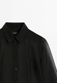 Musta läpinäkyvä paita, jossa on rakenteellinen kaulus, neljä mustaa nappia, hienovarainen vaakasuora tekstuuri ja pehmeät, valuvaa hihat.