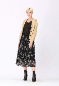 Cardigan beige avec des boutons noirs, top en dentelle noire, et une jupe noire à volants avec des motifs floraux argentés ; bottines noires.