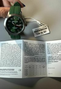 Orologio con cinturino in silicone verde, cassa argentata, quadrante verde scuro, grandi marker delle ore e lancetta dei secondi rossa. Include scheda di garanzia con i dettagli.