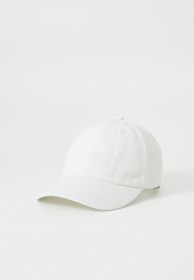 Witte katoenen pet met een licht gebogen rand, voorzien van reliëftekst op de voorkant en een genaaide ventilatieopening bovenaan.