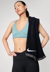 Svijetloplava sportska grudnjak i crne tajice visokog struka. Crni ručnik prebačen preko ramena sa bijelim Nike logom. Glatka tekstura.