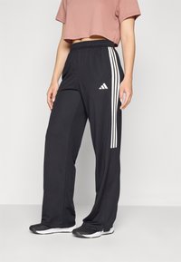 Svarta idrottsbyxor med elastisk midja, vita sidostripes med tre ränder och en Adidas-logotyp på vänster lår. Slät tygtextur.