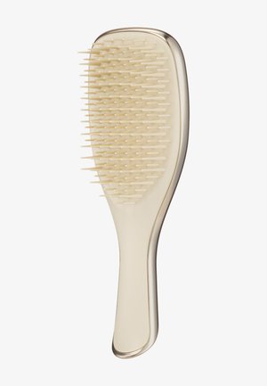 Brosse à cheveux en plastique beige avec un manche courbé et des poils flexibles serrés sur une tête ovale plate.