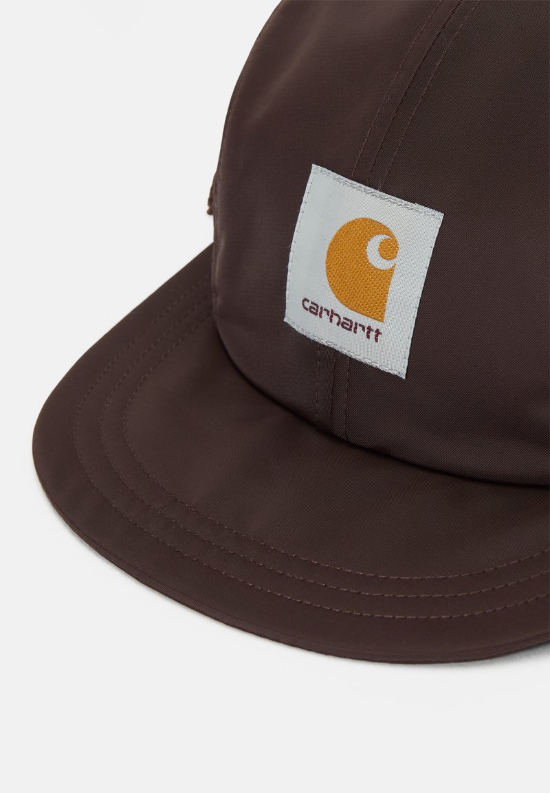 Brun kasket lavet af slidstærkt stof, med en flad skygge og et rektangulært logopatch med et gult design. Syninger er synlige langs sømmene.