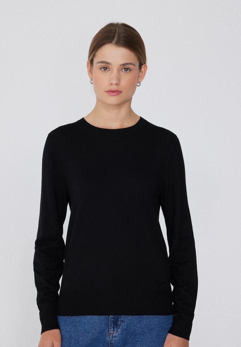 Schwarzer langärmliger Pullover aus weichem Strickmaterial mit Rundhalsausschnitt, schlanker Passform und gerippten Bündchen und Saum, getragen über blauen Jeans.