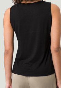 Sort ærmeløs top lavet af blød bomuld; glat tekstur med en rundet halsudskæring og en let buet kant forneden bagpå.