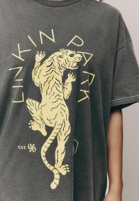 T-shirt oversize gris charbon avec un graphique de tigre jaune et le texte "LINKIN PARK" ainsi que "EST 96" en bas. Texture douce.