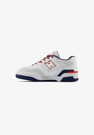 Chaussure de sport blanche avec des accents rouges et bleu marine, design à lacets, tige en cuir texturé et semelle en caoutchouc avec des rainures de traction.