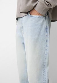 Lyseblå denimjeans med lige snit, præget af subtile falmede områder og et klassisk fem-lomme design. Synlige stikninger.
