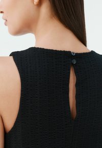 Černý top bez rukávů z texturované látky, s knoflíkovým zapínáním na zádech a malým výřezem ve tvaru klíče.