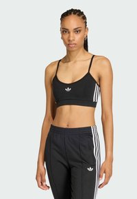 Čierny športový podprsenka s tenkými ramienkami, s bielym logom v strede. V páre s čiernymi nohavicami, ktoré majú biele bočné pruhy a vrecká.