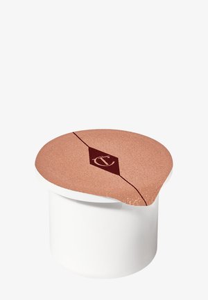 Pot cosmétique blanc avec un couvercle en feuille d'or rose affichant un logo noir en forme de losange avec les lettres "CT" au centre.