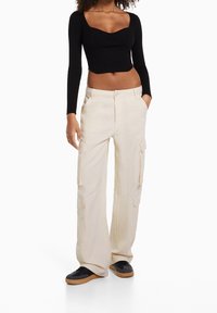 Černý žebrovaný dlouhý rukáv crop top spárovaný s béžovými cargo kalhotami, které mají boční kapsy, volný střih a rovný siluetu.