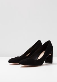 Décolleté in suede nero con punta affusolata e tacco grosso. L'interno presenta una fodera liscia, che mette in mostra un design minimalista.