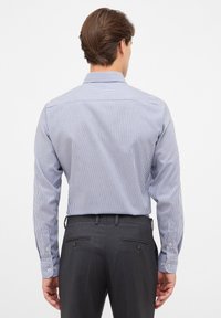 Camicia a righe bianche e blu navy con maniche lunghe, polsini con bottoni e colletto classico, abbinata a pantaloni grigi su misura.